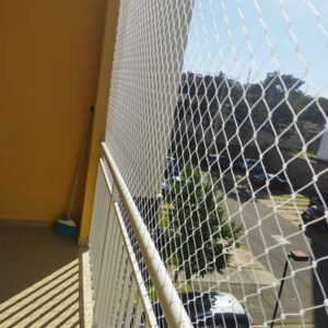 Detalhe da instalação de tela de proteção em uma varanda de prédio em Curitiba, com a cidade ao fundo, ideal para proteção infantil.